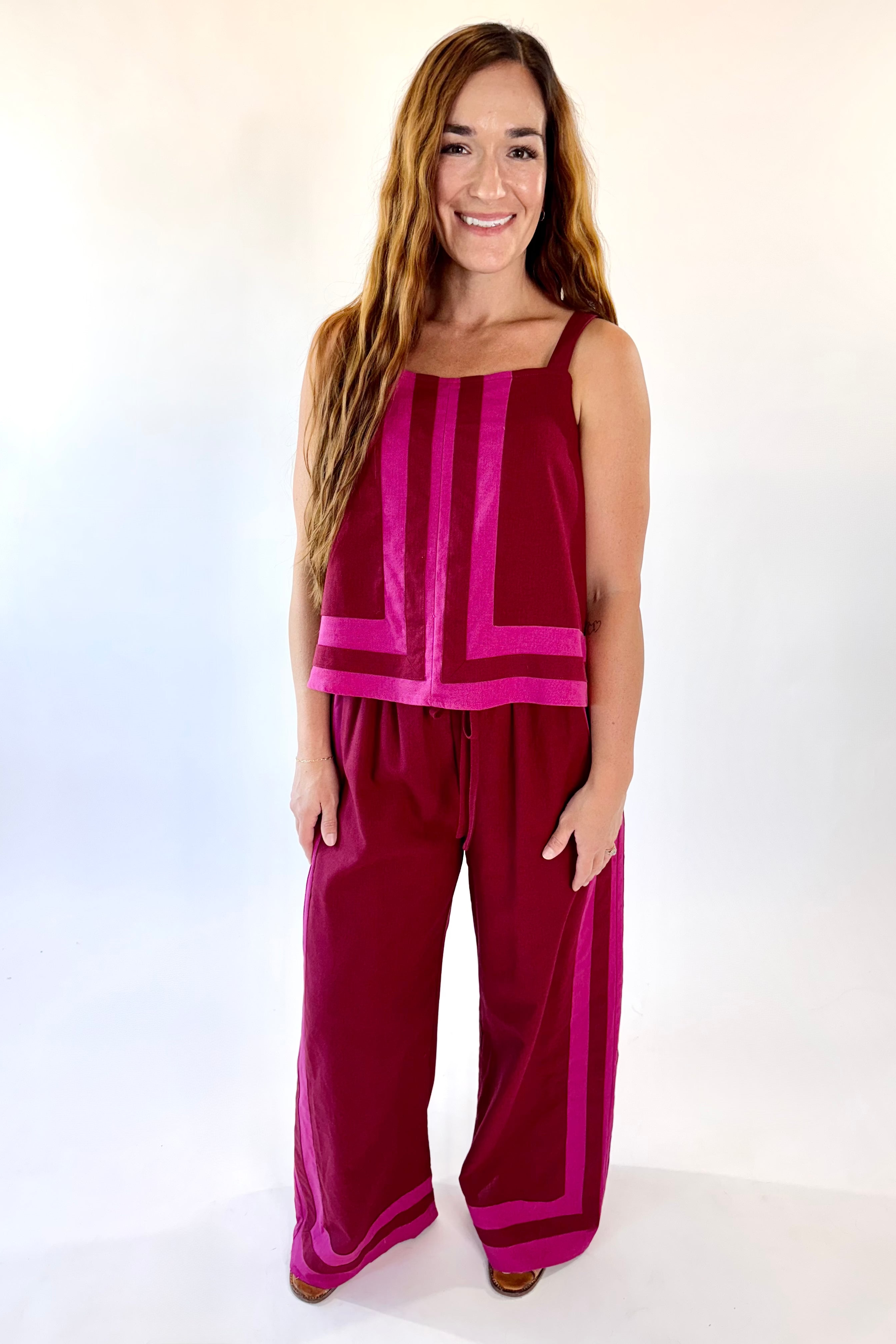 Woman wearing a magenta sleeveless top and wide-leg pants on a white background