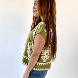 Woman wearing a green top with white patterns and blue jeans on a white background