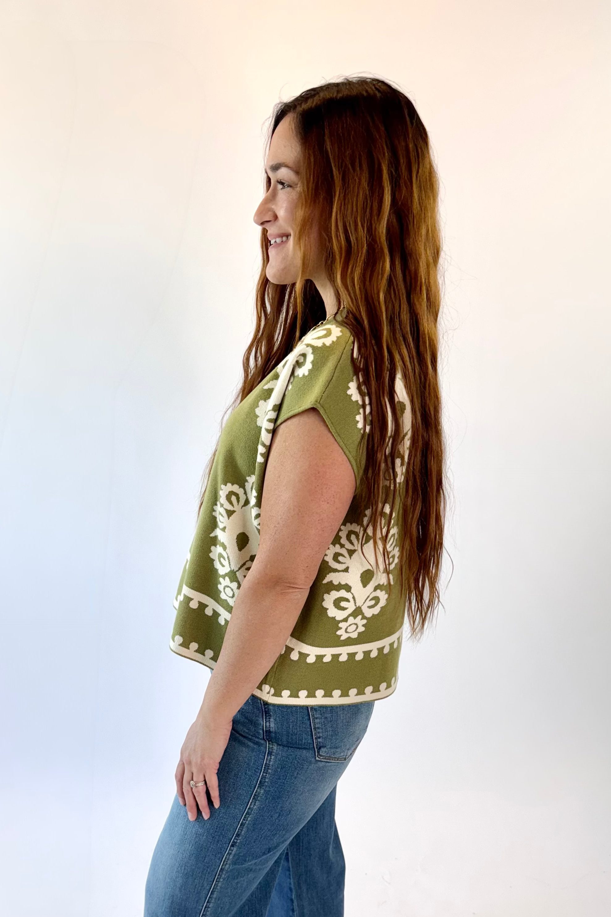 Woman wearing a green top with white patterns and blue jeans on a white background