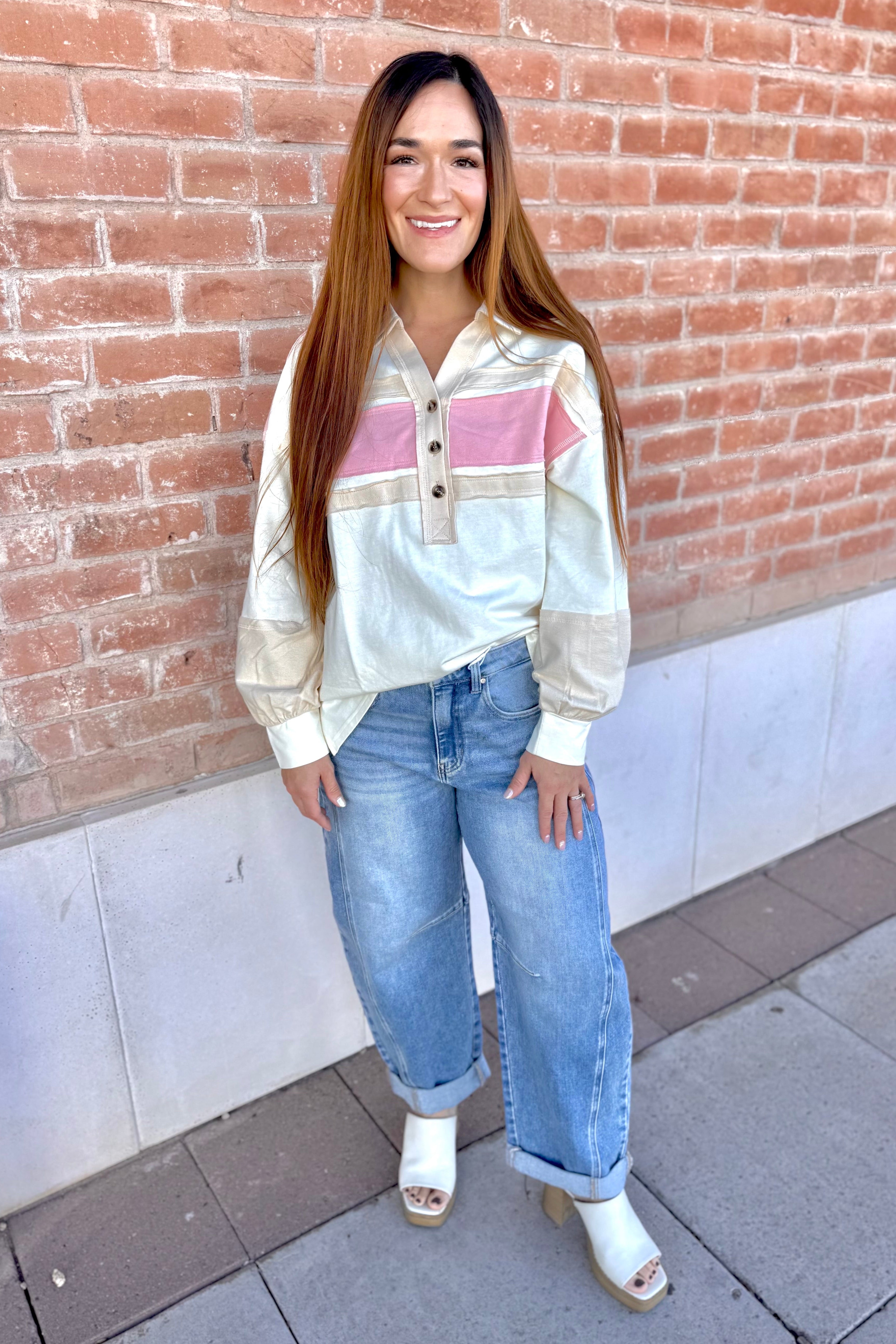 Woman wearing a striped shirt and jeans standing against a brick wall.