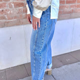 Person wearing a light-colored top and blue jeans standing against a brick wall.