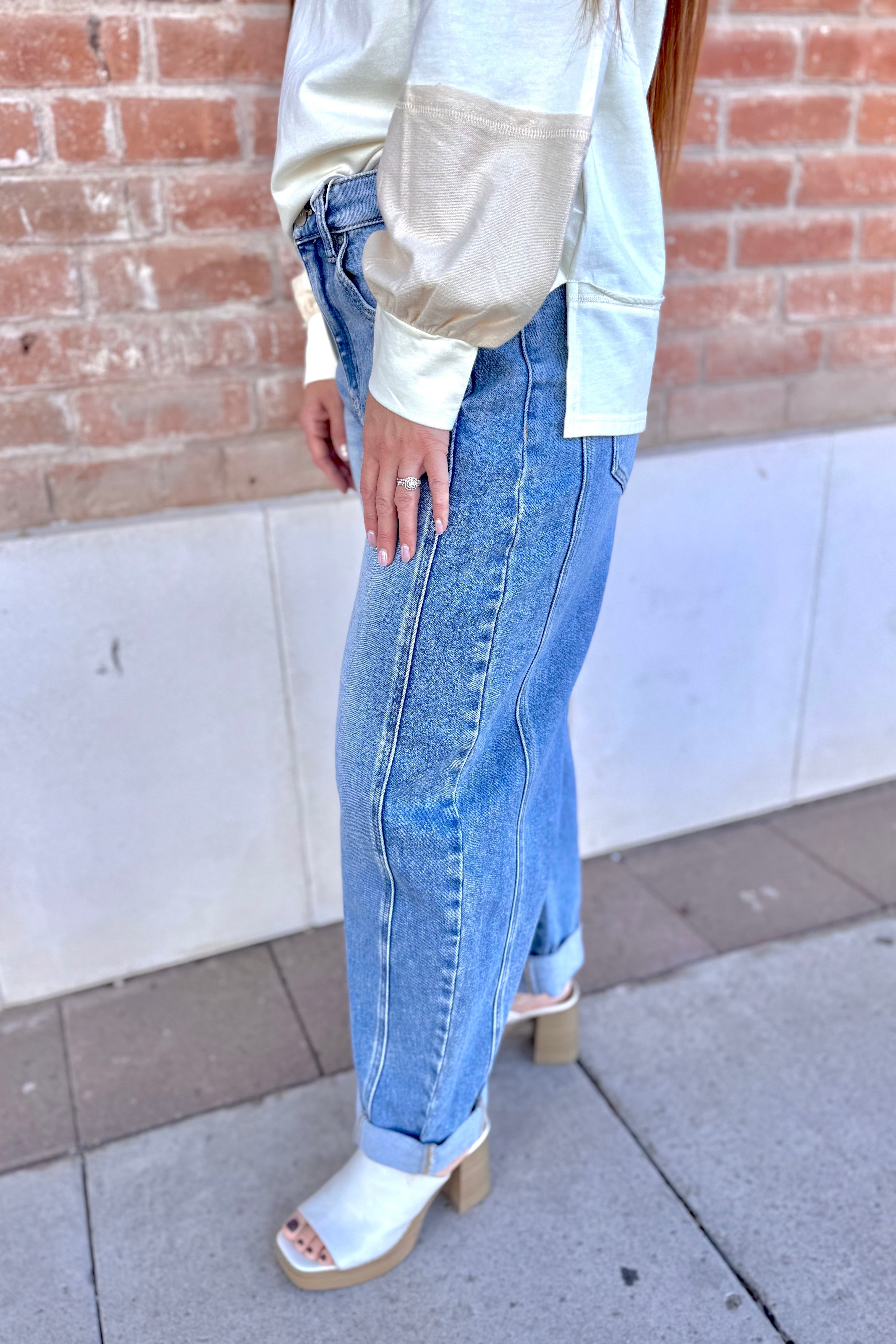 Person wearing a light-colored top and blue jeans standing against a brick wall.