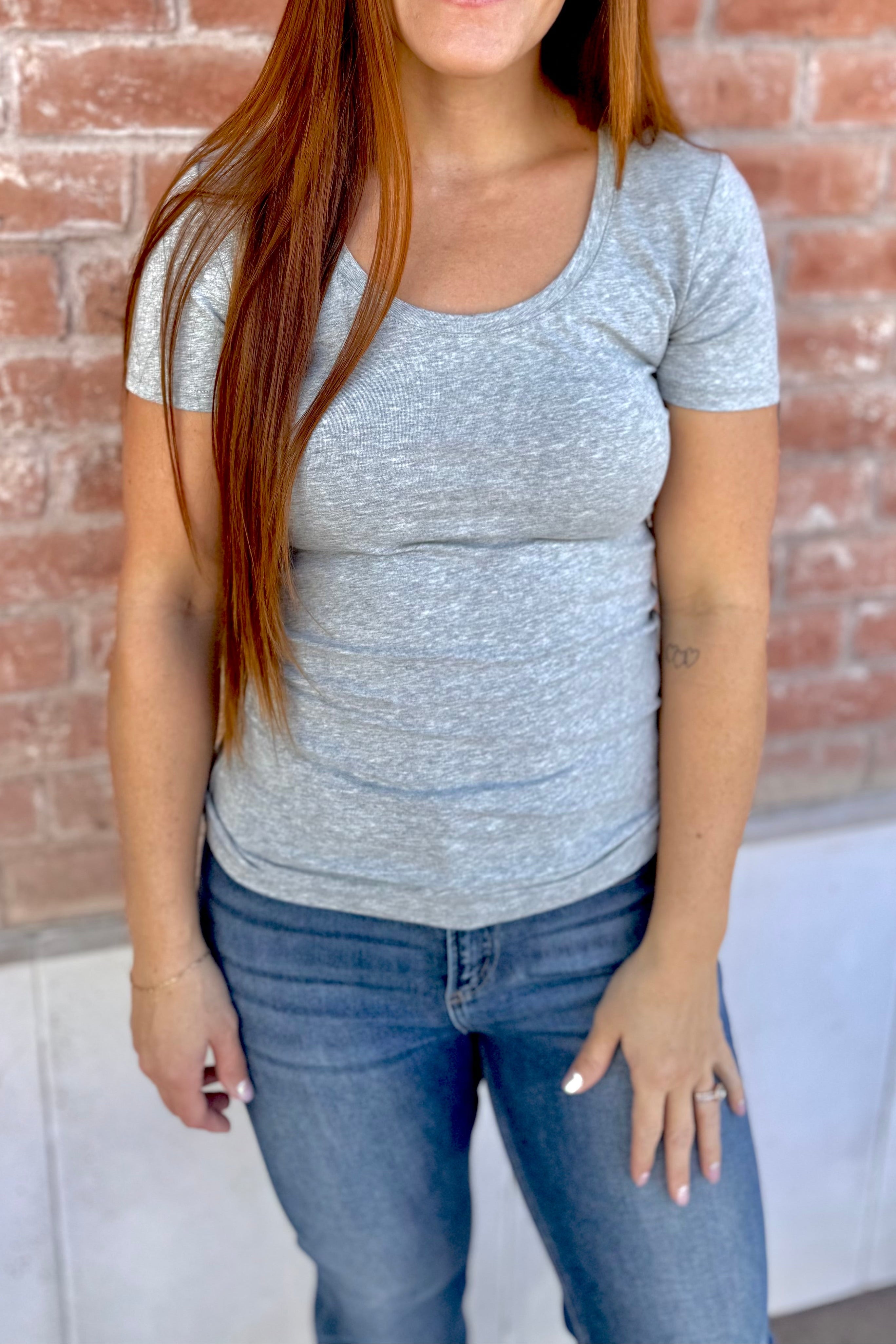 Woman wearing a gray t-shirt and blue jeans standing in front of a brick wall.