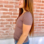 Woman wearing a brown t-shirt and blue jeans standing against a brick wall.