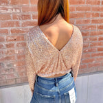 Person wearing a sparkly top and blue jeans against a brick wall.