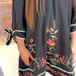 Black dress with floral embroidery and tied sleeves worn by a person.