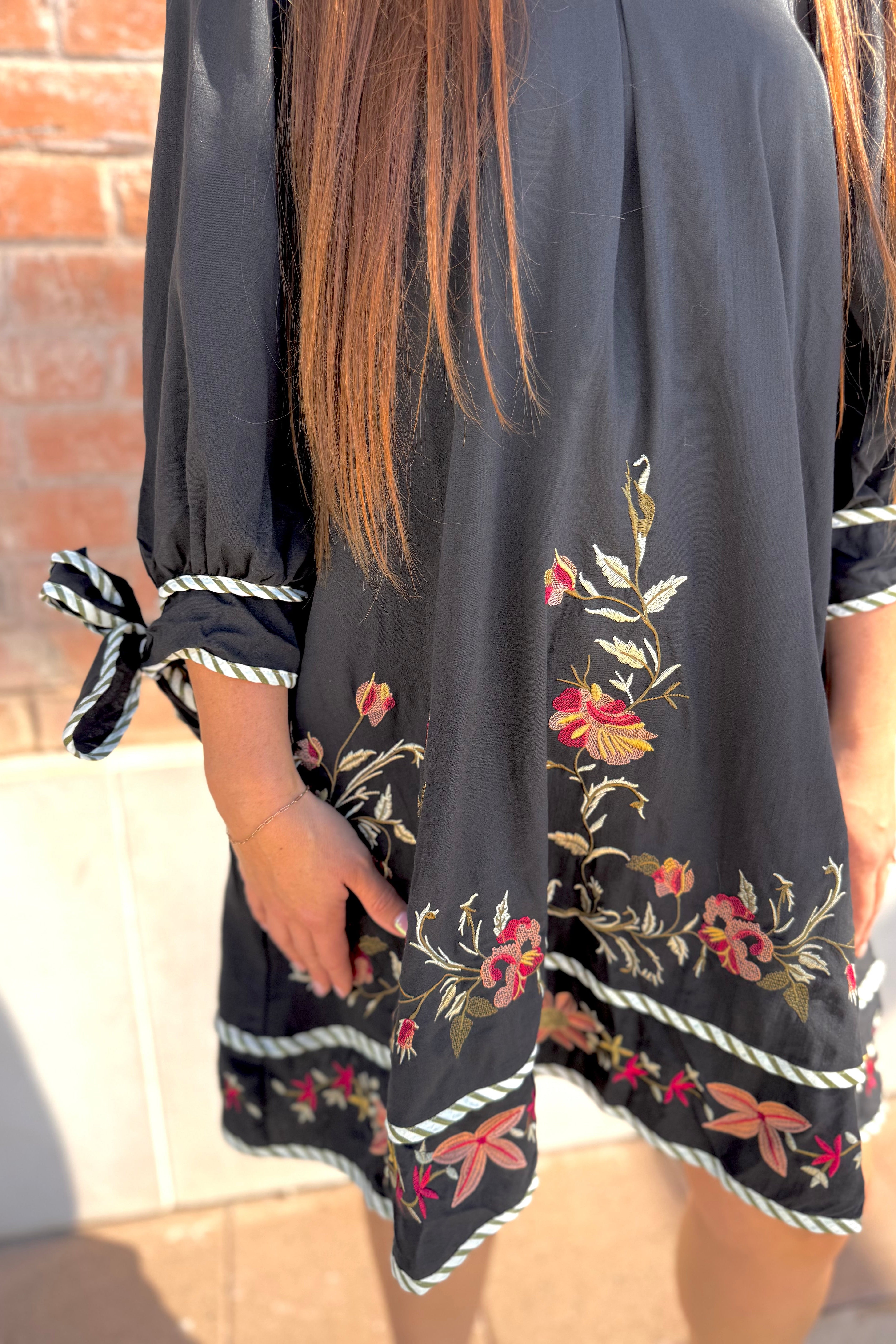 Black dress with floral embroidery and tied sleeves worn by a person.