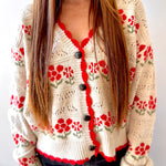 Person wearing a cream-colored cardigan with red floral patterns on a white background