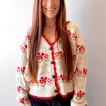 Woman wearing a beige cardigan with red floral patterns against a plain background