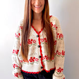 Woman wearing a beige cardigan with red floral patterns against a plain background