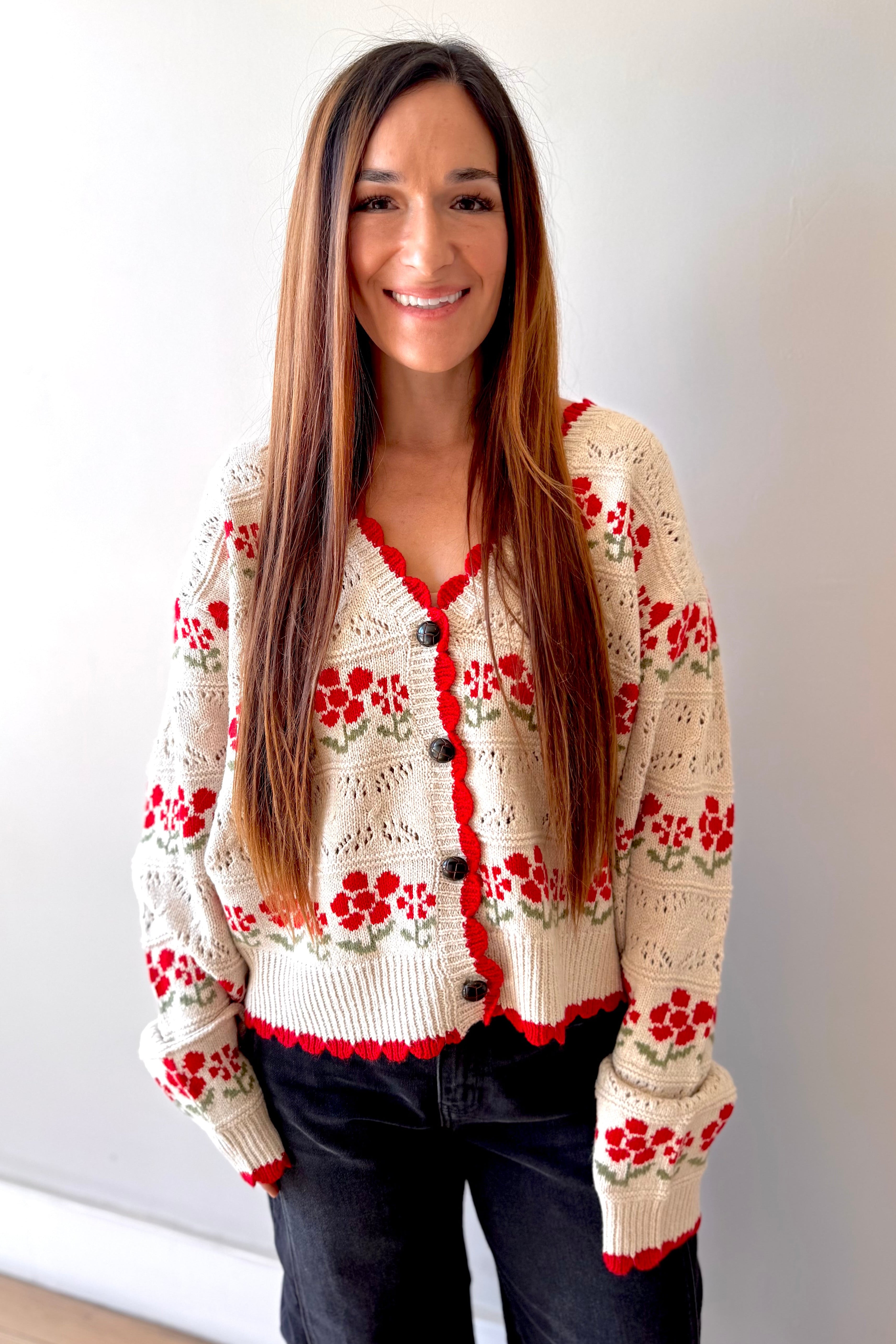 Woman wearing a beige cardigan with red floral patterns against a plain background