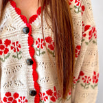 Close-up of a person wearing a cream-colored cardigan with red floral patterns and black buttons.