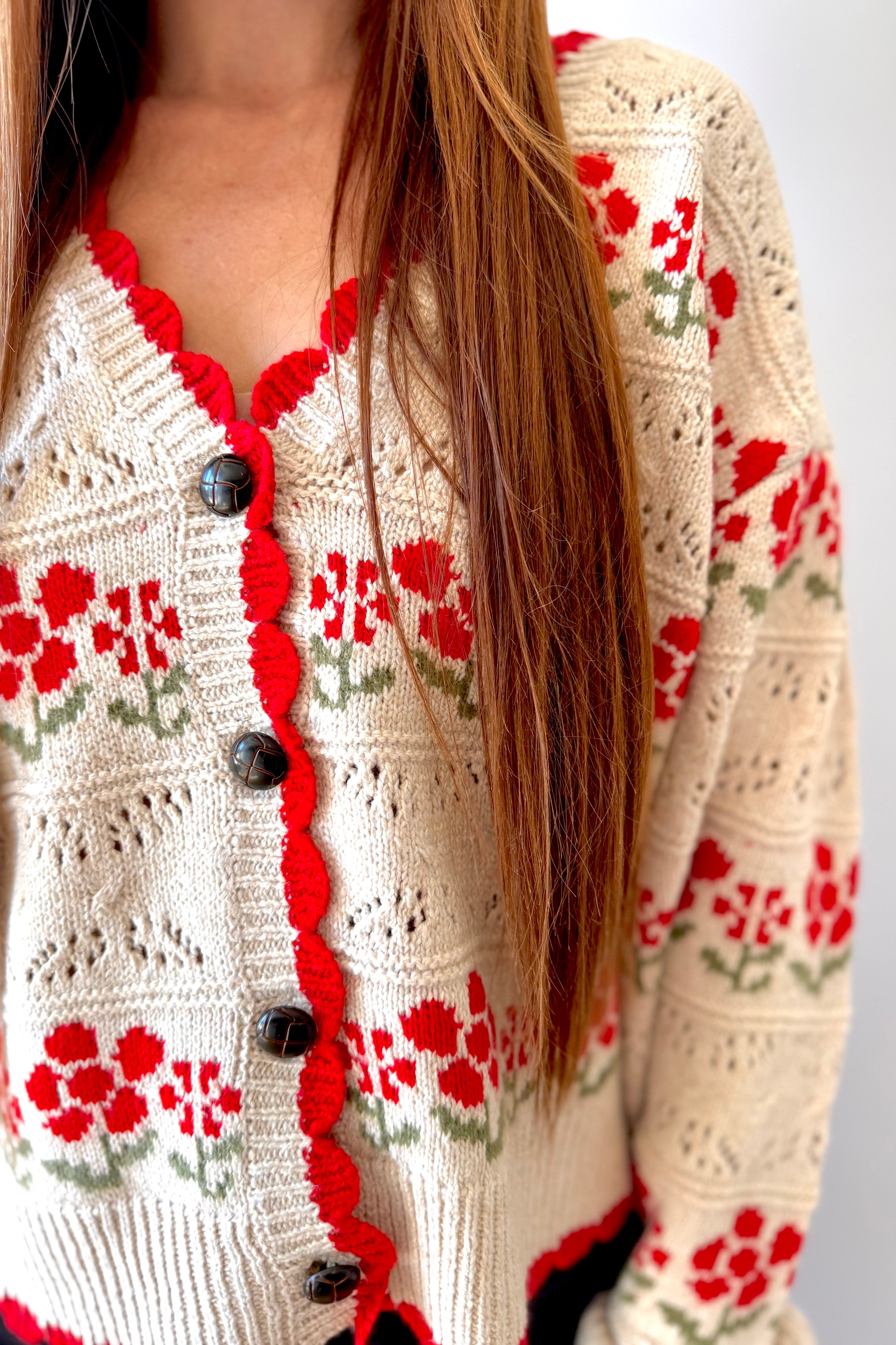 Close-up of a person wearing a cream-colored cardigan with red floral patterns and black buttons.