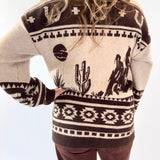Person wearing a patterned sweater with cactus and cowboy design on a white background