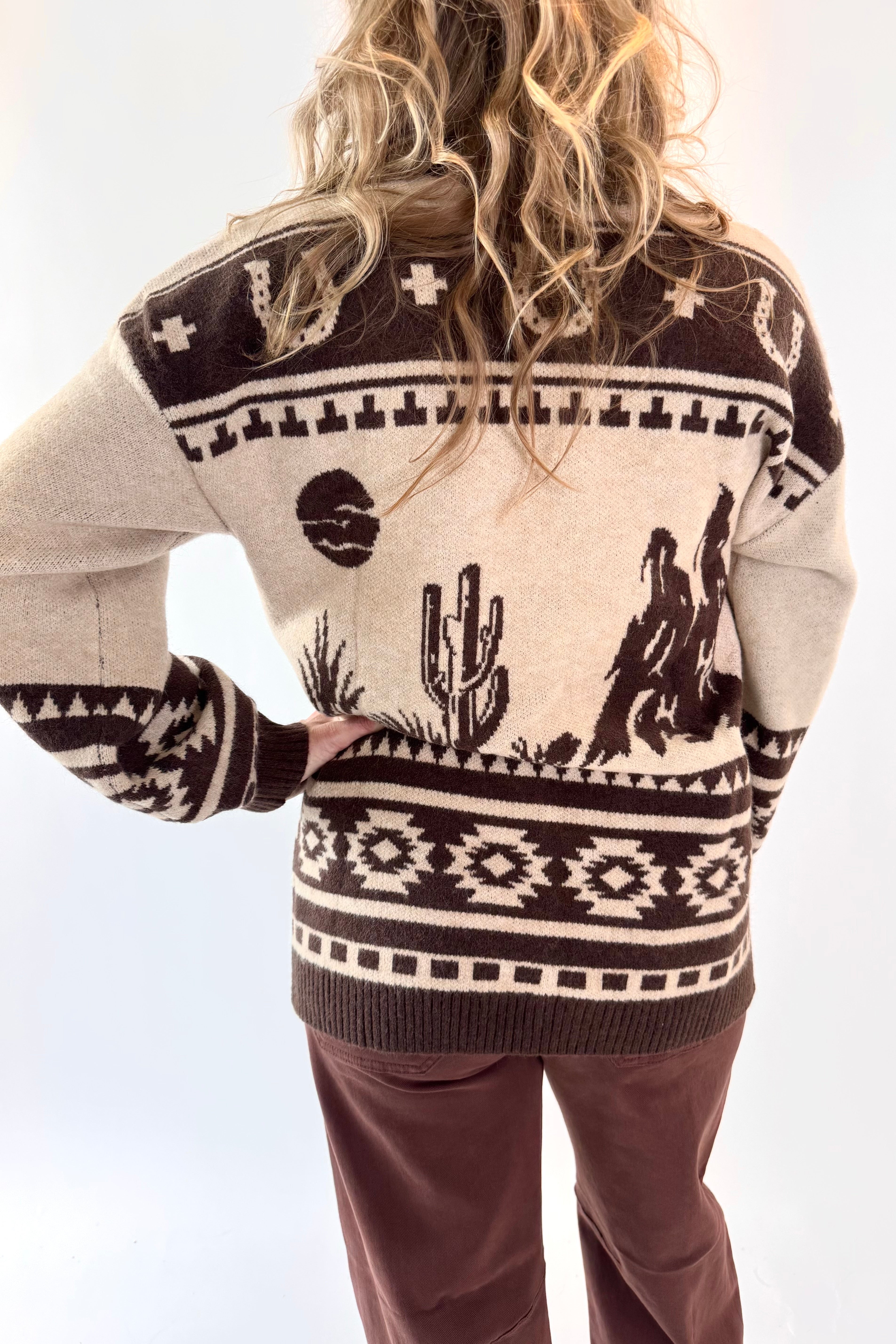 Person wearing a patterned sweater with cactus and cowboy design on a white background