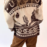 Person wearing a patterned sweater with desert-themed designs on a white background