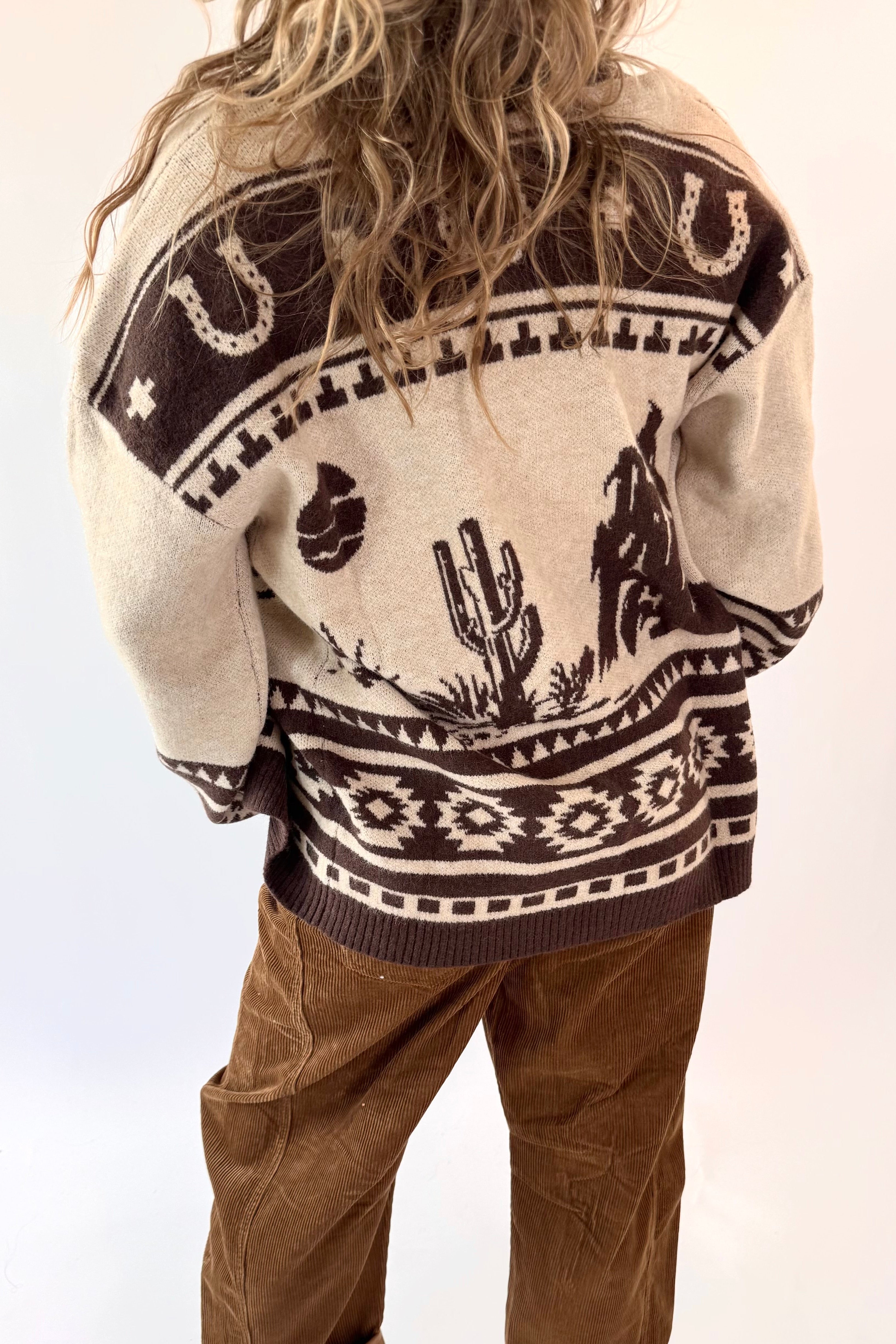 Person wearing a patterned sweater with desert-themed designs on a white background