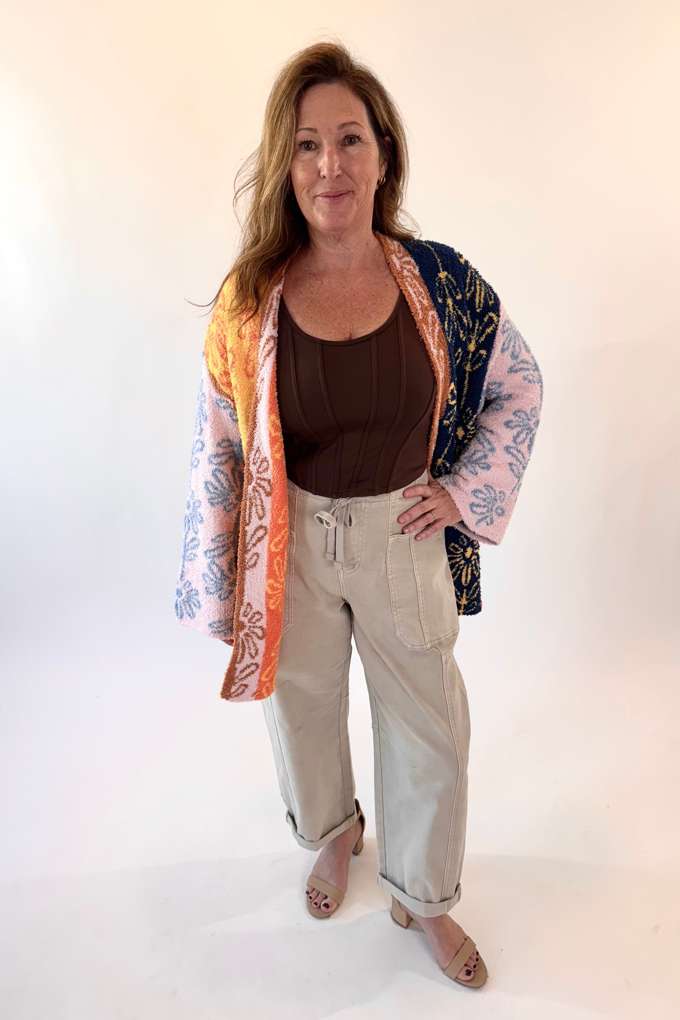 Woman wearing a colorful kimono-style jacket over a brown top and beige pants on a white background