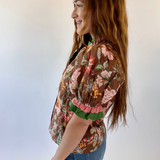 Woman wearing a floral blouse and jeans against a plain background