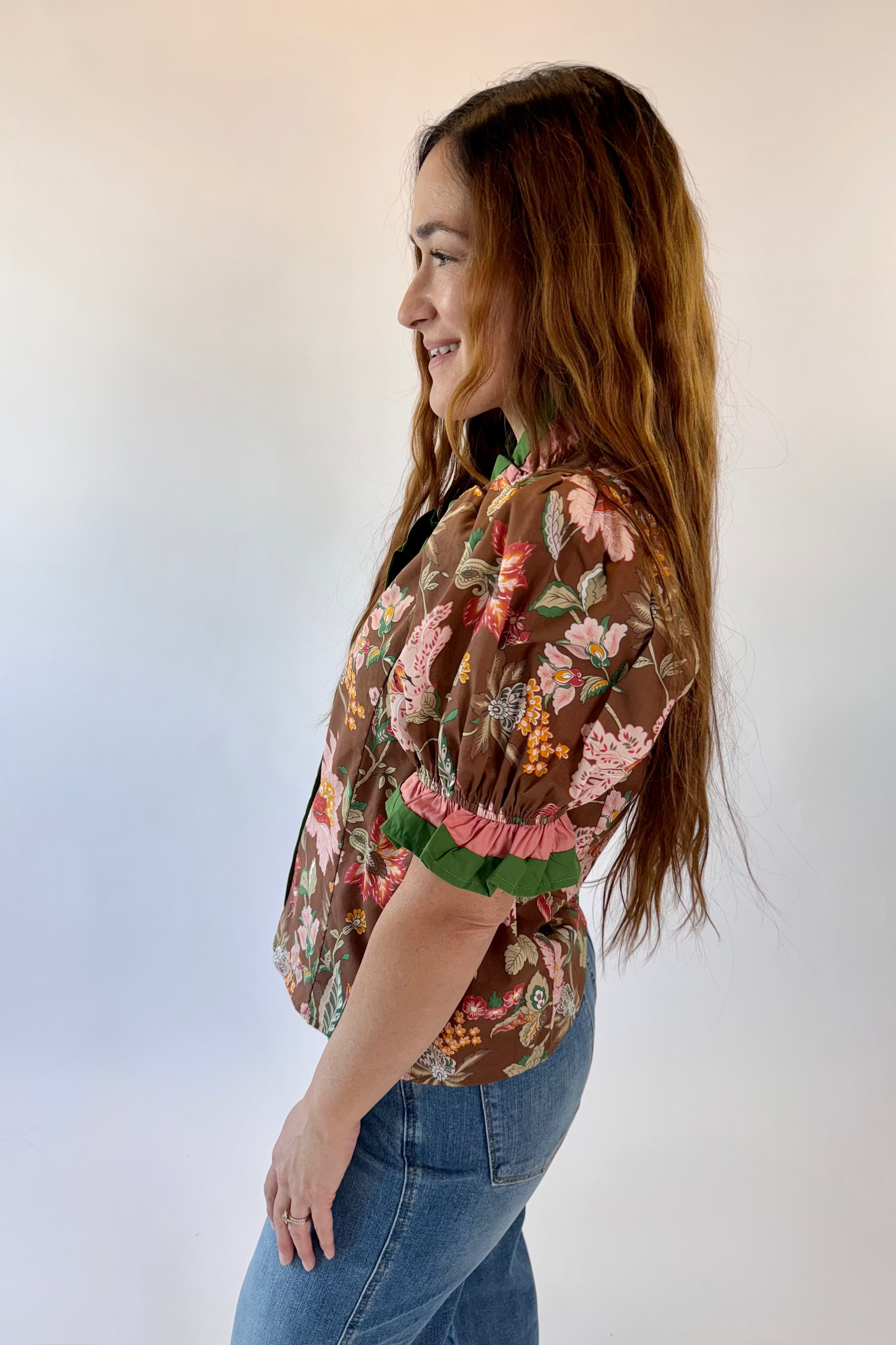 Woman wearing a floral blouse and jeans against a plain background