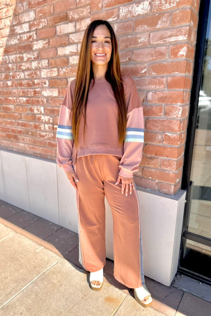Woman in a pink and brown outfit standing against a brick wall.