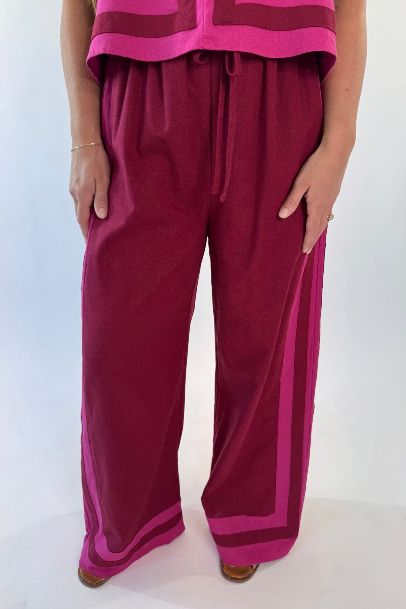 Maroon pants with pink accents worn by a person on a white background
