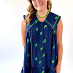 Young girl wearing a navy dress with green and red patterns on a white background