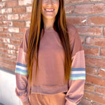 Woman wearing a brown sweatshirt and pants standing against a brick wall.