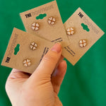 Three pairs of earrings on 'The Boutique' cards held by a hand against a green background
