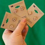 Three pairs of earrings on 'The Boutique' cards held by a hand against a green background
