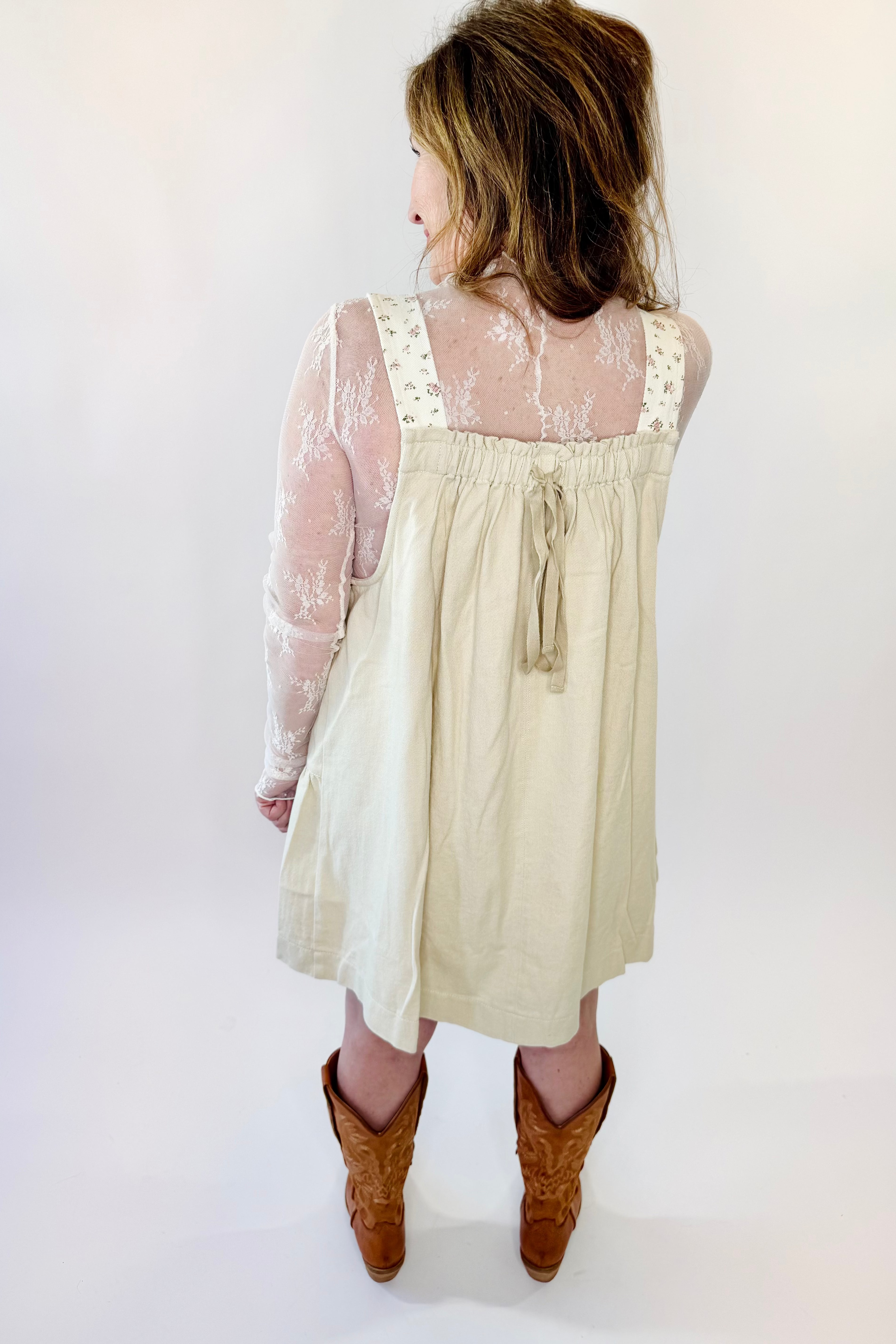Woman wearing a beige dress with sheer sleeves against a white background