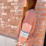 Woman in a peach-colored outfit with striped pants standing against a brick wall.
