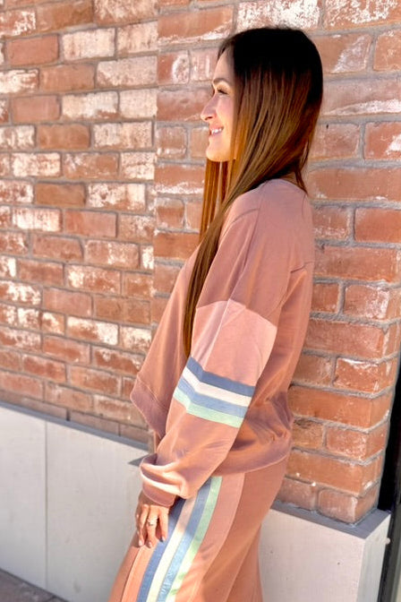 Woman in a peach-colored outfit with striped pants standing against a brick wall.