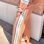 Woman in a peach-colored outfit with striped pants standing against a brick wall.