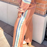 Woman in a peach-colored outfit with striped pants standing against a brick wall.