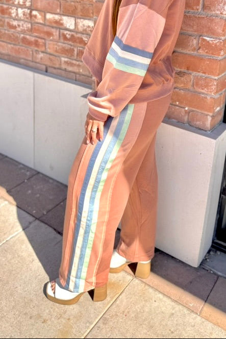 Woman in a peach-colored outfit with striped pants standing against a brick wall.