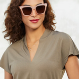 Woman wearing pink sunglasses and a green top against a plain background