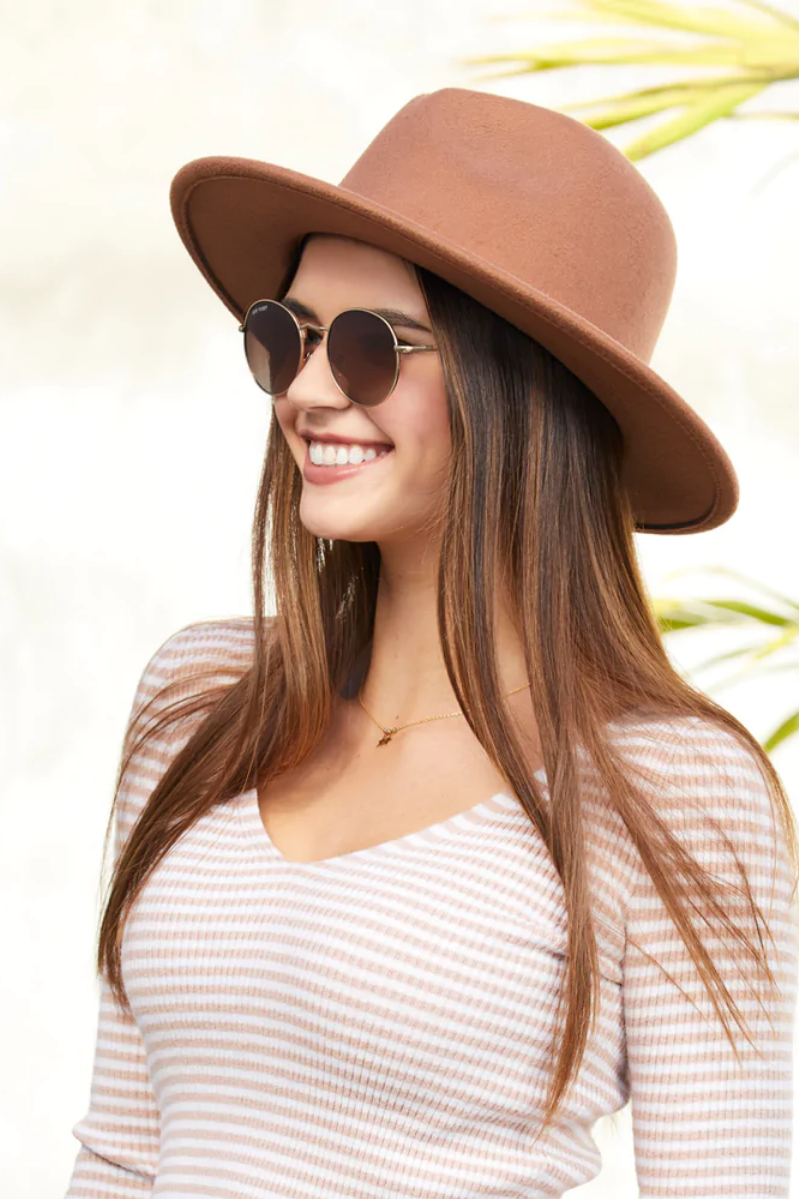 Woman wearing a brown hat and sunglasses with a blurred natural background