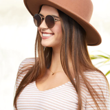 Woman wearing a brown hat and sunglasses with a blurred natural background