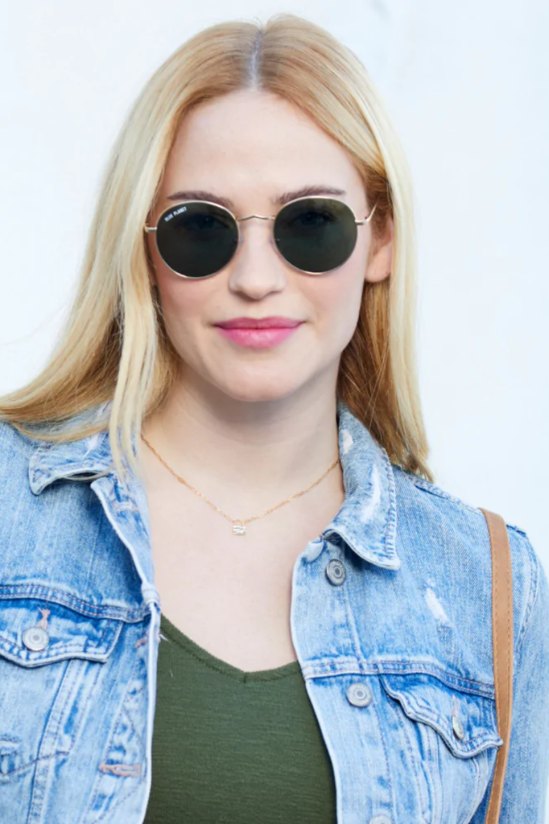Woman wearing sunglasses and a denim jacket against a light background