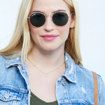 Woman wearing sunglasses and a denim jacket against a light background