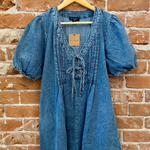 Blue denim dress on a hanger against a brick wall