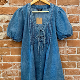 Blue denim dress on a hanger against a brick wall