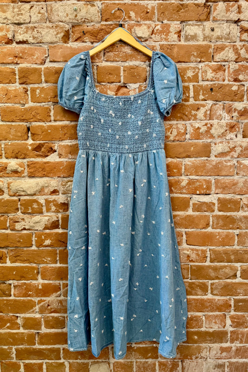 Blue dress with ruffled sleeves on a hanger against a brick wall.