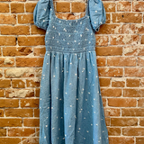 Blue dress with ruffled sleeves on a hanger against a brick wall.