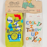 Two baby socks with humorous text on a Blue Q packaging label. 2 Pack saying: "Big Fan of Shapes & Colors", "Cool If I throw Up on You?"