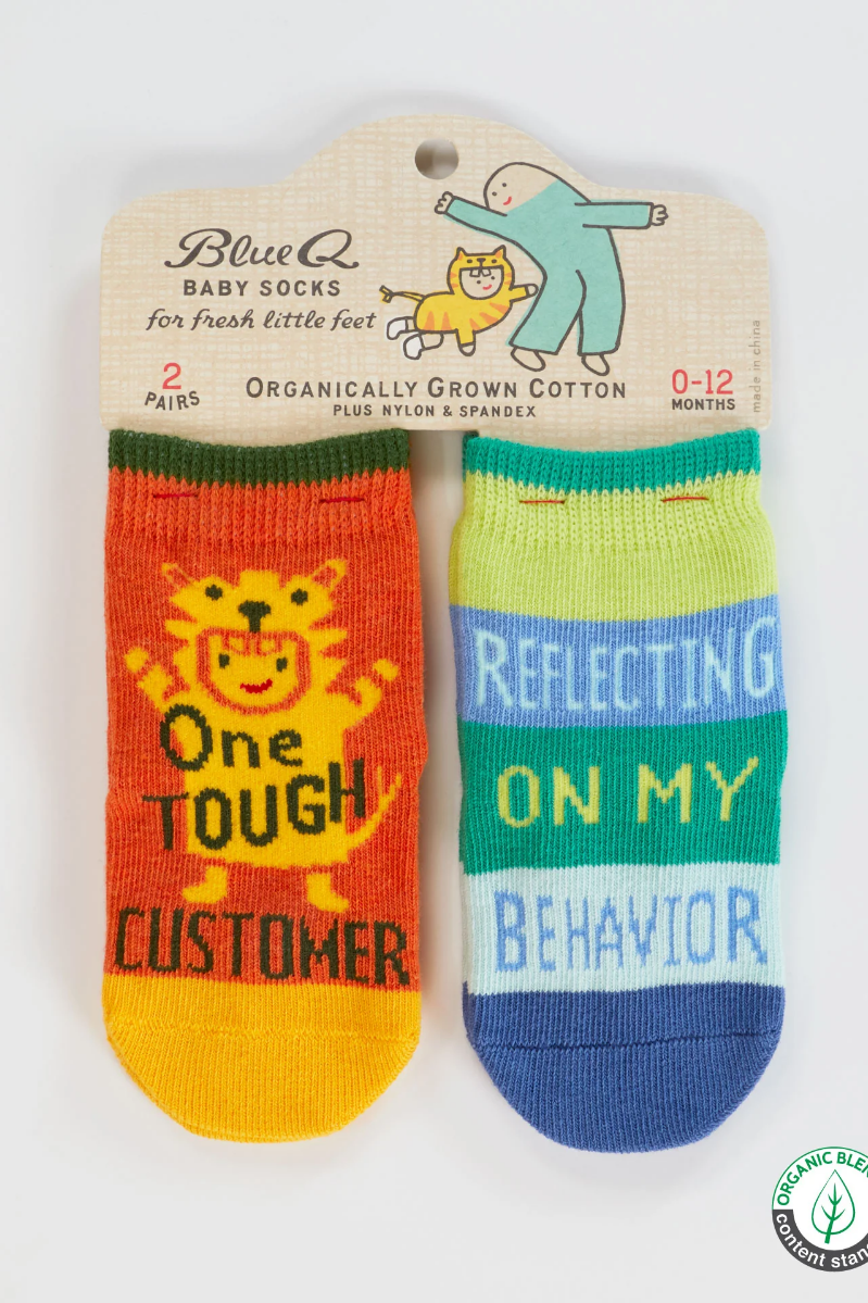 Two baby socks with text on a Blue Q packaging. "One Tough Customer", "Reflecting On My Behavior" Baby Socks.
