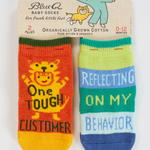 Two baby socks with text on a Blue Q packaging. "One Tough Customer", "Reflecting On My Behavior" Baby Socks.