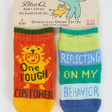 Two baby socks with text on a Blue Q packaging. "One Tough Customer", "Reflecting On My Behavior" Baby Socks.
