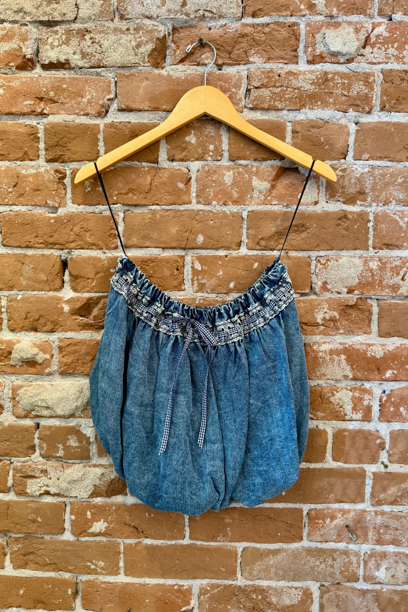 Blue denim dress with lace details on a wooden hanger against a brick wall.